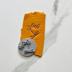 Photo of a clay stamp for polymer clay earrings and jewelry, representing an orchid flower. In the photo is also a sample of mustard clay textured with the same stamp. 