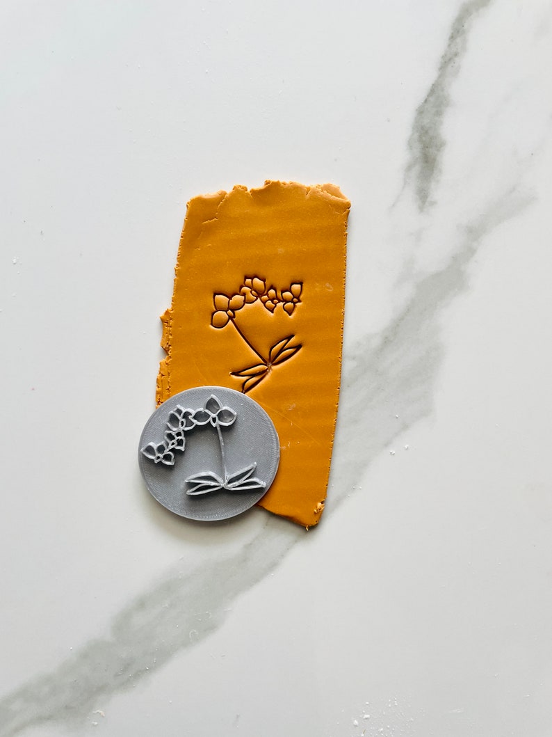 Photo of a clay stamp for polymer clay earrings and jewelry, representing an orchid flower. In the photo is also a sample of mustard clay textured with the same stamp. 