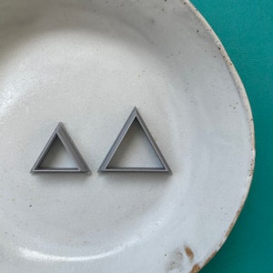 May include: Two silver triangle-shaped cookie cutters on a white ceramic plate.