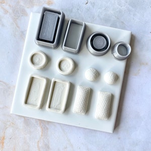 Może przedstawiać: Zestaw 12 białych i szarych form z polimerowej gliny do tworzenia biżuterii. Formy są ułożone na białej powierzchni płytek. Formy mają różne kształty, w tym koła, kwadraty i prostokąty.