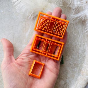 May include: Set of four orange plastic cookie cutters shaped like windows. The cutters are in different sizes and styles, including a double window with diamond-shaped panes.