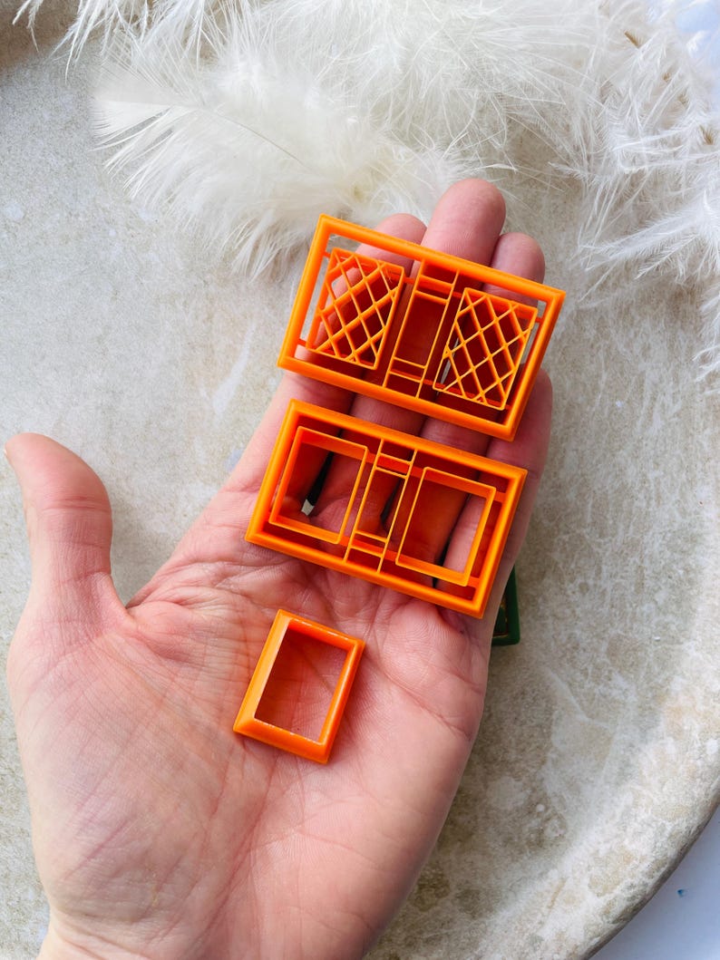 May include: Set of four orange plastic cookie cutters shaped like windows. The cutters are in different sizes and styles, including a double window with diamond-shaped panes.