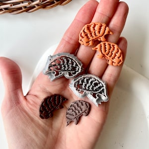 Op de afbeelding: Vijf kleine, gedetailleerde dierenkoekjesvormen. Twee zijn oranje, twee zijn bruin en één is grijs. De vormen zijn in de vorm van gordeldieren.