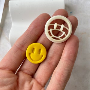 May include: A white plastic smiley face cookie cutter and a yellow smiley face cookie.