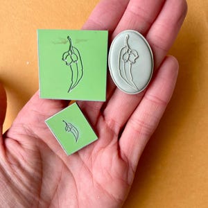 May include: Three rubber stamps with a green background and a black outline of a eucalyptus branch with leaves and buds. The stamps are in different sizes and shapes, including a square, a rectangle, and an oval.