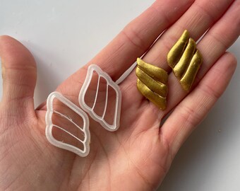 Peut inclure: Deux ensembles d'objets en forme d'ailes. L'un est blanc et en plastique, l'autre est doré. Les ailes dorées ont un aspect texturé et métallique. Les ailes blanches sont un moule ou un emporte-pièce, et les ailes dorées semblent être des produits finis.