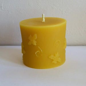 May include: A yellow beeswax candle with a decorative design of flowers and bees. The candle is cylindrical and has a smooth surface.