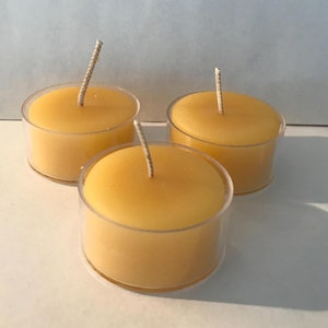 Puede incluir: Tres velas de té amarillas en recipientes de plástico transparente. Las velas tienen mechas blancas.