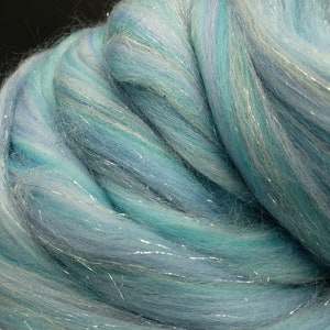 K&ouml;nnte beinhalten: Nahaufnahme eines B&uuml;ndels blauer und wei&szlig;er Wollroving mit silbernen Schimmerf&auml;den. Der Roving ist weich und flauschig, und die Farben sind leuchtend.