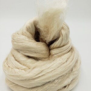 Peut inclure: Un gros amas de fibres naturelles blanc cass&eacute;, probablement de la soie ou de la laine, avec quelques brins de fibres blanches qui d&eacute;passent.