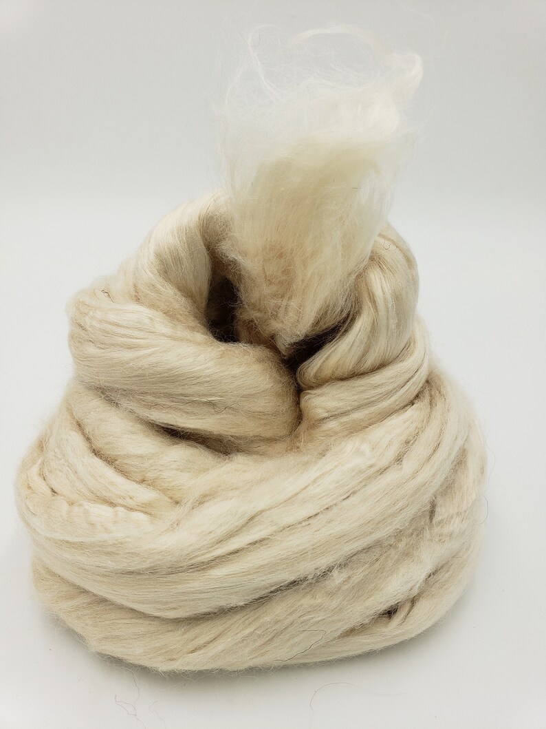 Peut inclure: Un gros amas de fibres naturelles blanc cass&eacute;, probablement de la soie ou de la laine, avec quelques brins de fibres blanches qui d&eacute;passent.