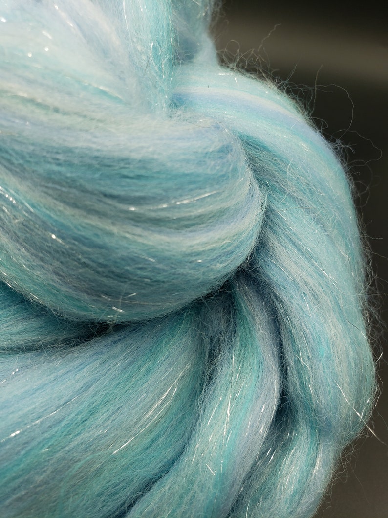 K&ouml;nnte beinhalten: Nahaufnahme eines B&uuml;ndels hellblauer und wei&szlig;er Wolle mit silbernen Glitzerf&auml;den, die durch die gesamte Wolle gewebt sind.