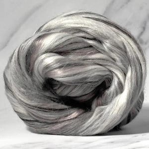Könnte beinhalten: Ein eng gewickelter Ball aus Fasern in Grau-, Weiß- und Schwarztönen. Die Faser hat ein weiches, strukturiertes Aussehen mit subtilen rosa Farbtönen. Das Material ist wahrscheinlich Wolle oder ein ähnliches Textil, das sich zum Spinnen oder für andere Bastelprojekte eignet.