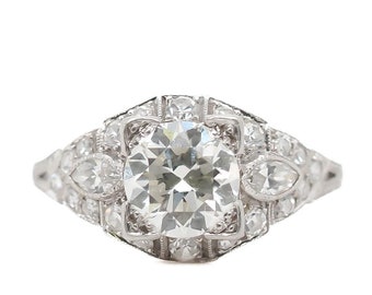 Könnte beinhalten: Ein silberner Ring mit einem großen runden Diamanten, der von kleineren Diamanten umgeben ist. Der Ring hat ein zartes Design mit einem floralen Motiv.