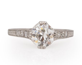 May include: A silver ring with a large, round, clear diamond in the center. The band is set with smaller diamonds.