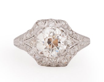 May include: A vintage platinum engagement ring with a large round brilliant cut diamond surrounded by smaller diamonds in a halo setting.