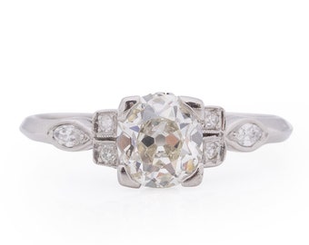 Könnte beinhalten: Ein silberner Ring mit einem großen, runden, klaren Diamanten in der Mitte. Der Diamant ist von kleineren Diamanten in einer filigranen Fassung umgeben.