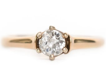Puede incluir: Un anillo de compromiso de oro con un solo diamante redondo engastado en una garra de cuatro puntas.