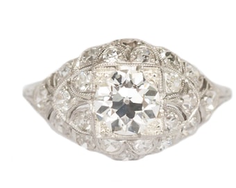 May include: A silver ring with a large, round, clear diamond surrounded by smaller diamonds. The ring has a delicate, intricate design.