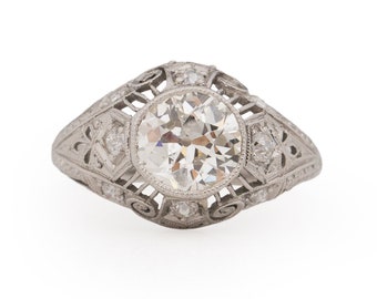 May include: A vintage platinum engagement ring with a round brilliant cut diamond center stone and a delicate filigree design.