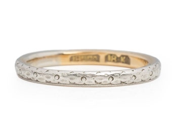 May include: A thin, gold and white wedding band with a textured design. The band is inscribed with "IRK" on the inside.