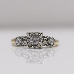 May include: A gold ring with a central diamond surrounded by smaller diamonds. The ring has a delicate, vintage style.