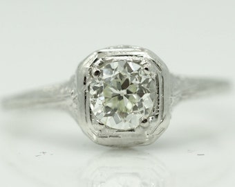 May include: A vintage engagement ring featuring a round brilliant cut diamond set in a platinum setting. The ring has a delicate filigree design on the band.