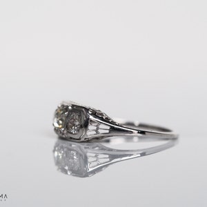 May include: A silver engagement ring with a single, round, clear diamond set in a filigree design.
