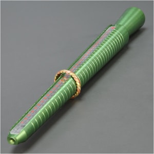 May include: A green ring sizer with a metal ring on it. The sizer has a scale marked in numbers.