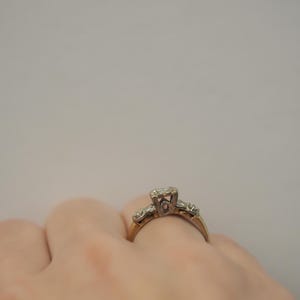 May include: A gold ring with a single diamond in the center and smaller diamonds on the band. The ring is on a person's finger.