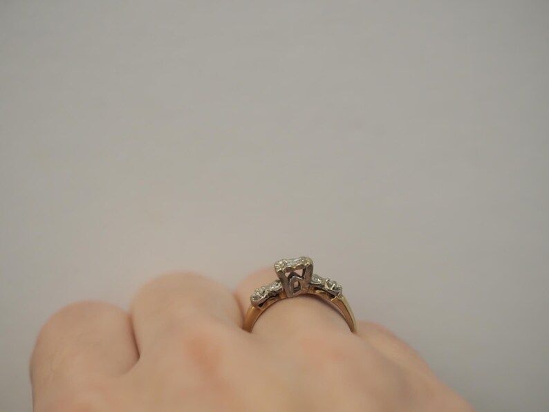 May include: A gold ring with a single diamond in the center and smaller diamonds on the band. The ring is on a person's finger.