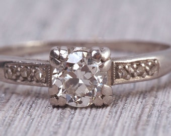 May include: A silver engagement ring with a single round diamond set in a prong setting. The band is decorated with smaller diamonds.
