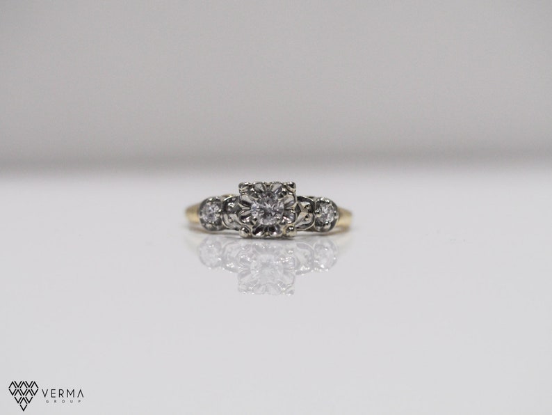 May include: A gold ring with a central diamond surrounded by smaller diamonds. The ring has a delicate, vintage style.