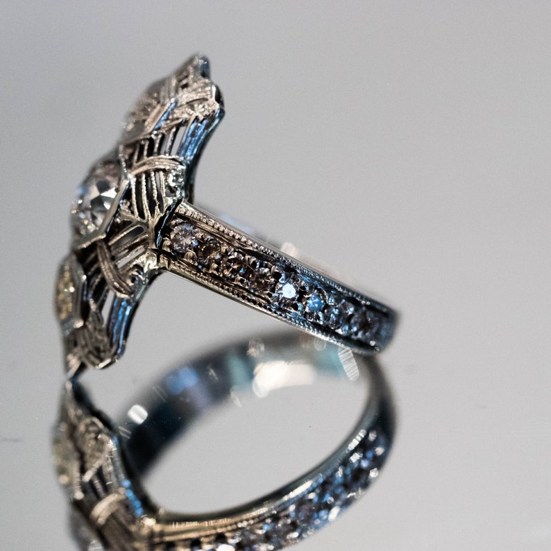 May include: A silver ring with a large, faceted gemstone surrounded by smaller gemstones. The ring has a delicate, intricate design.