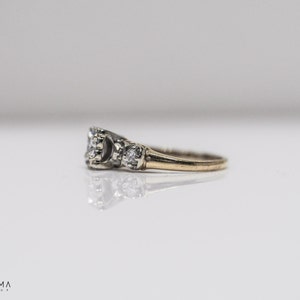 May include: A gold band ring with three round diamonds. The center diamond is larger than the two side diamonds.