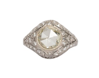 Könnte beinhalten: Ein Ring im Vintage-Stil mit einem großen, runden, hellgelben Diamanten als Mittelstein. Der Ring ist in einem silberfarbenen Metall mit aufwendigen Details und kleineren Diamanten gefasst. Der Ring ist vor einem weißen Hintergrund abgebildet.