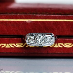 May include: A silver ring with three round diamonds set in a three-prong setting. The ring is in a red velvet box.