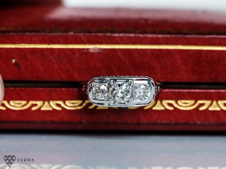 May include: A silver ring with three round diamonds set in a three-prong setting. The ring is in a red velvet box.