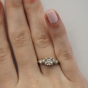 May include: A gold ring with a large round diamond in the center and two smaller diamonds on either side.