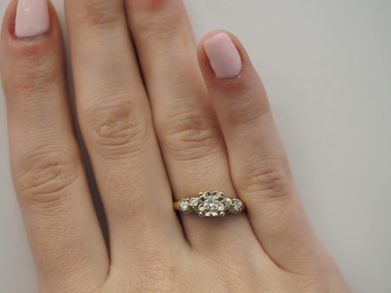 May include: A gold ring with a large round diamond in the center and two smaller diamonds on either side.