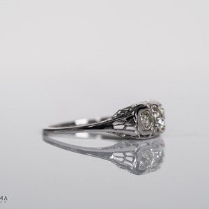 May include: A silver ring with two round diamonds set in a delicate filigree design.