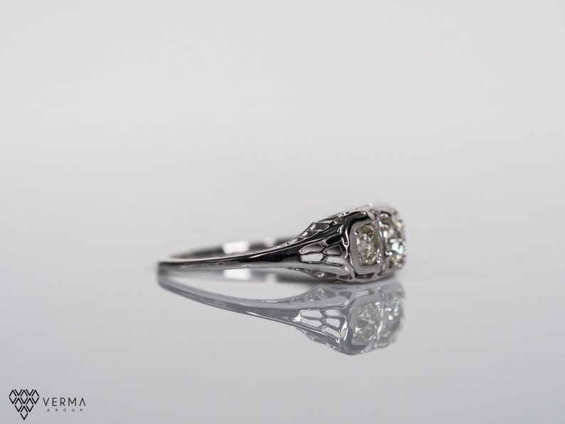 May include: A silver ring with two round diamonds set in a delicate filigree design.
