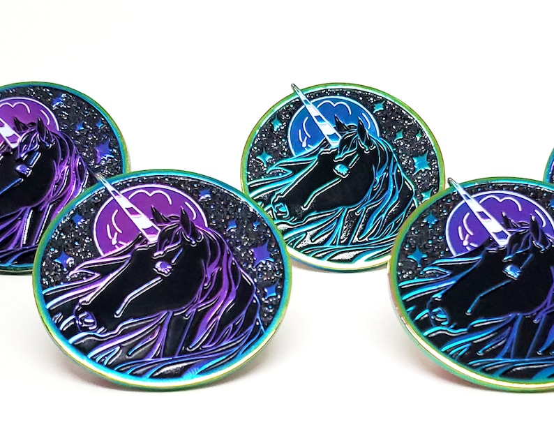 May include: Four iridescent enamel pins featuring a black unicorn with a white horn against a dark blue background with a purple moon and white stars.