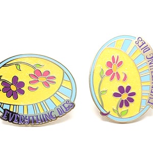 K&ouml;nnte beinhalten: Zwei Emaille-Anstecknadeln mit floralem Design und dem Text "EVERYTHING DIES". Die Anstecknadeln haben einen gelben Hintergrund mit rosa und lila Blumen, einen hellblauen Rand und eine silberne Metallkontur. Der Text ist in lila Schrift.