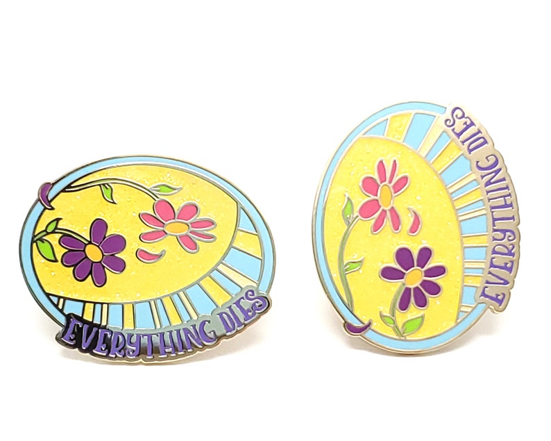 K&ouml;nnte beinhalten: Zwei Emaille-Anstecknadeln mit floralem Design und dem Text "EVERYTHING DIES". Die Anstecknadeln haben einen gelben Hintergrund mit rosa und lila Blumen, einen hellblauen Rand und eine silberne Metallkontur. Der Text ist in lila Schrift.
