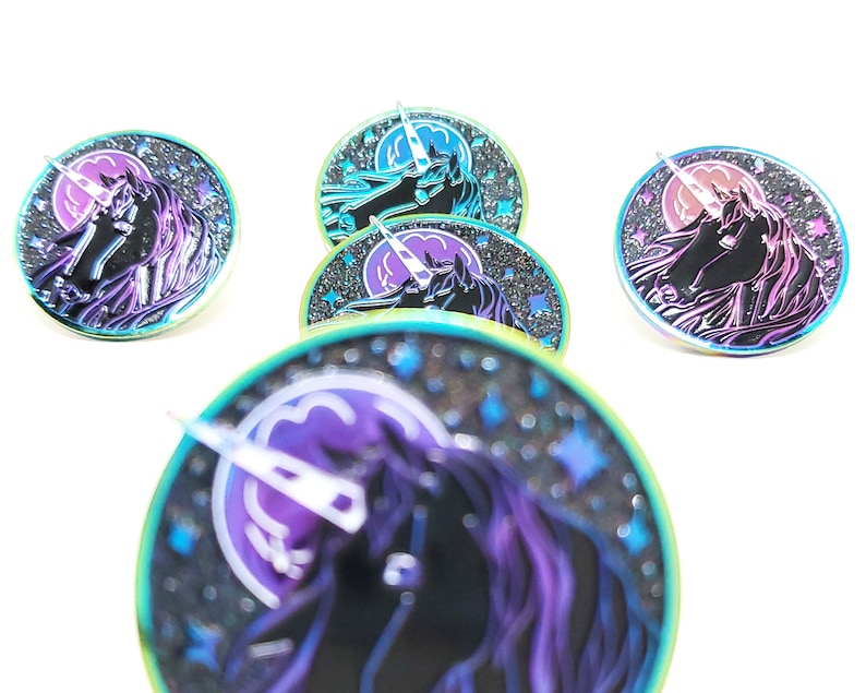 May include: Five iridescent enamel pins featuring a black unicorn with a rainbow horn and a crescent moon in the background. The pins have a sparkly, glittery finish and are set against a white background.