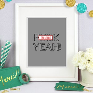 Puede incluir: Una impresi&oacute;n enmarcada en blanco con un fondo gris y el texto "F censurado K YEAH!" en negro. La impresi&oacute;n est&aacute; sobre una mesa con una tarjeta verde que dice "Merci!" en letras doradas.