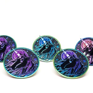 May include: Four iridescent enamel pins featuring a unicorn head silhouette against a black background with a crescent moon and stars. The unicorn's horn is white and the pins have a rainbow iridescent finish.