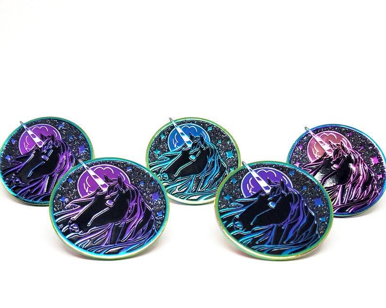 May include: Four iridescent enamel pins featuring a unicorn head silhouette against a black background with a crescent moon and stars. The unicorn's horn is white and the pins have a rainbow iridescent finish.