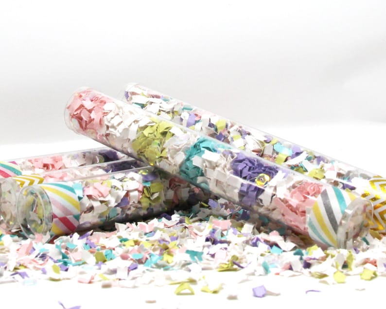 Puede incluir: Cuatro tubos de pl&aacute;stico transparente llenos de confeti de colores. El confeti es en tonos de rosa, morado, verde y blanco. Los tubos tienen un patr&oacute;n de rayas en la parte inferior.